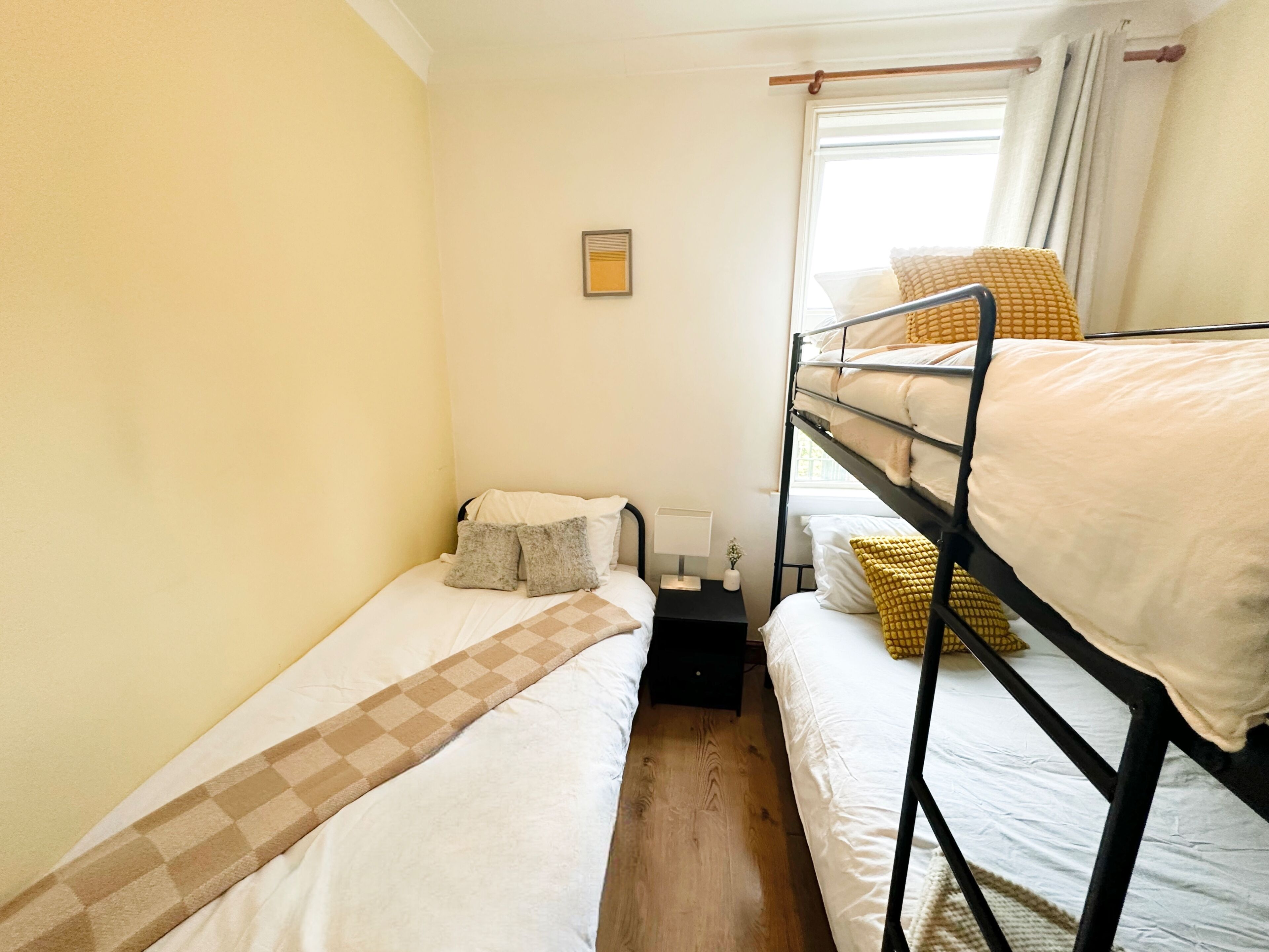 Un dormitorio con literas, una mesita de noche pequeña, una lámpara y una ventana con cortinas.