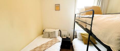 Un dormitorio con literas, una mesita de noche pequeña, una lámpara y una ventana con cortinas.