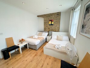 A modern hotel room with a brick accent wall, two beds, a small table with a vase, a chair, and a fan. - 11 Guests - 6min Drive to the Wembley Stadium (Wembley)