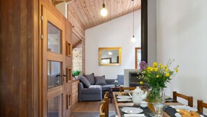 A cozy dining area with a wooden table set for two, a sofa in the background, and a mirror on the wall.