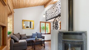 A cozy living room with a fireplace, wooden ceiling, and a sofa with cushions.
