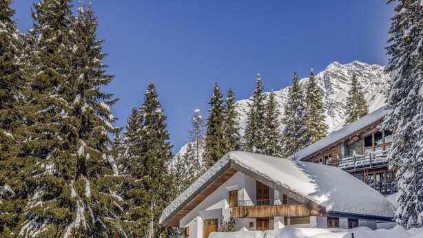 A snow-covered mountain lodge with a wooden exterior and a balcony overlooking the snowy landscape.