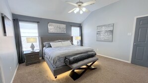 A bedroom with a bed, a ceiling fan, a nightstand, and a door. - Modern 4BR Retreat Extended Stay Ideal. SW Houston (Sugar Land)