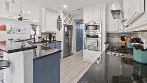 A modern kitchen with white cabinets, a central island, stainless steel appliances, and a blue door in the background. - Modern 4BR Retreat Extended Stay Ideal. SW Houston (Sugar Land)