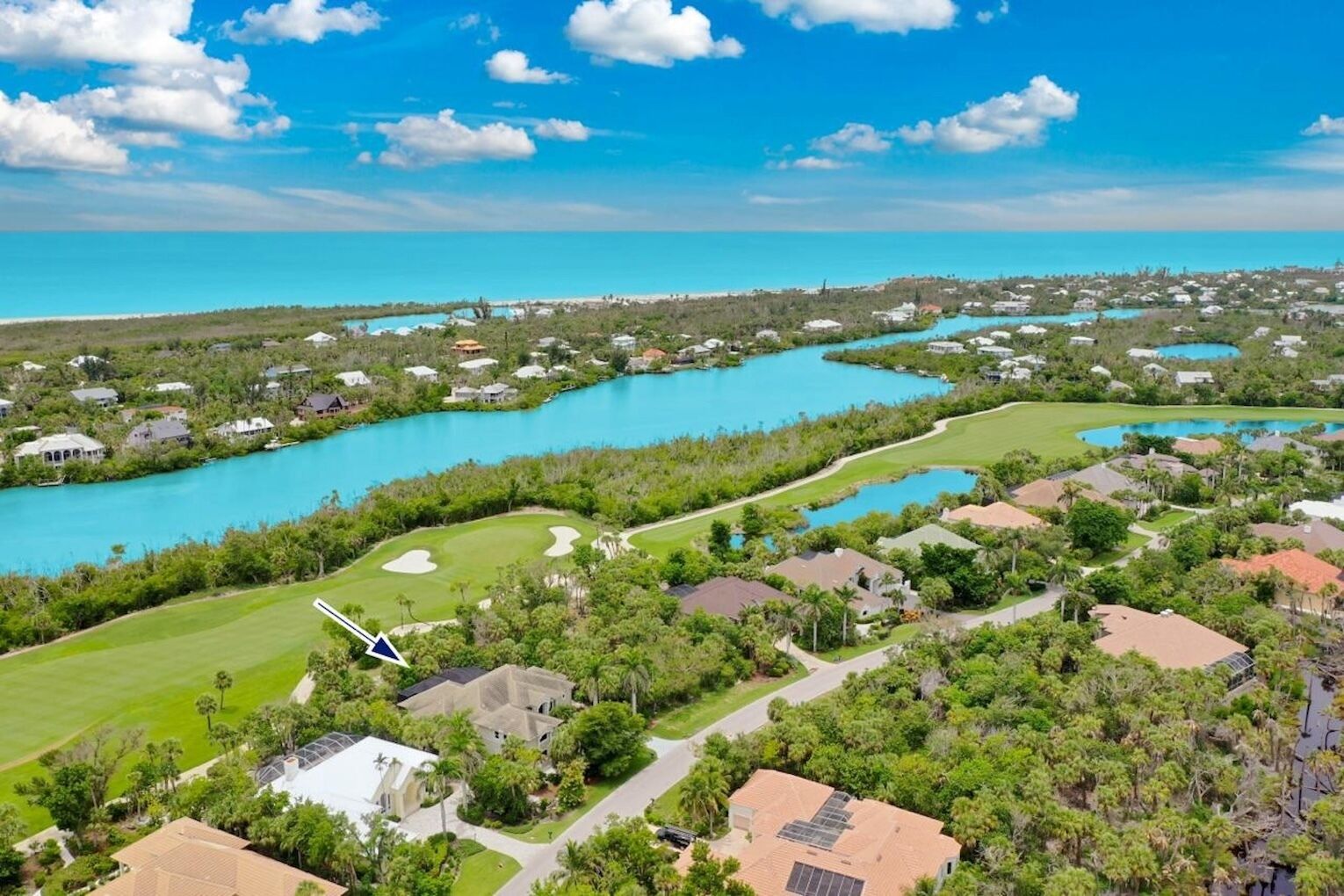 A coastal residential area with houses, a golf course, and a large body of water.
