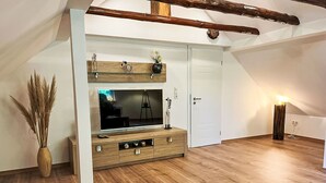 Een moderne woonkamer met een houten tv-meubel, een grote flatscreen televisie, een vaas met gedroogde planten en een houten vloer.