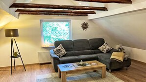Een gezellige woonkamer met een hoekbank, een salontafel, een vloerlamp en een raam met uitzicht op groen.