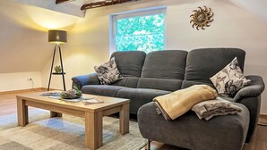 Een gezellige woonkamer met een grijze bank, een houten salontafel, een vloerlamp en een decoratief zon-symbool aan de muur.