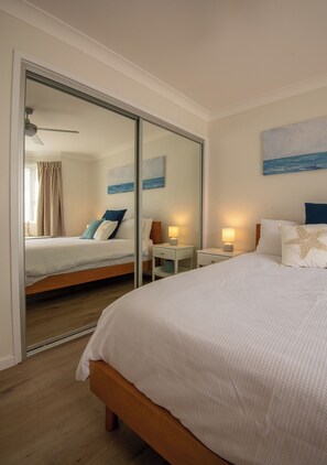 Habitación de hotel con una cama grande, una mesita de noche con lámpara, un espejo y un cuadro marino en la pared.
