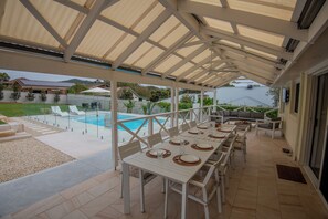 Un patio exterior con zona de comedor cubierta, piscina y vistas del paisaje circundante.