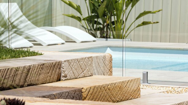 A pool area with stone steps leading into the water, surrounded by a white fence and greenery.