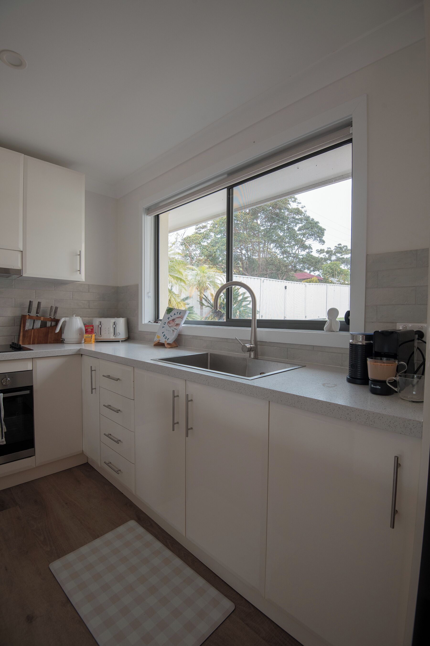Eine moderne Küche mit weißen Schränken, einer Edelstahl-Spüle, einem Fenster und Blick ins Freie.