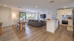 A modern kitchen with white cabinets, a built-in oven, and a dining area with a wooden table and white chairs.