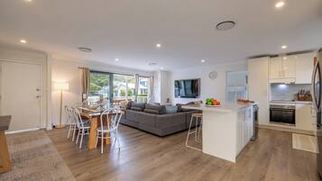 A modern kitchen with white cabinets, a built-in oven, and a dining area with a wooden table and white chairs.