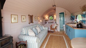 A cozy, well-lit room with a striped sofa, a small dining table, and a kitchen area with a sink and kettle. - Wonderful  villa for 4 guests with hot tub, terrace and pets allowed (Banbury)