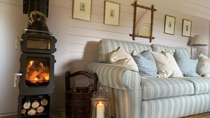 A cozy room with a wood-burning stove, a striped sofa, and a lantern. - Wonderful  villa for 4 guests with hot tub, terrace and pets allowed (Banbury)