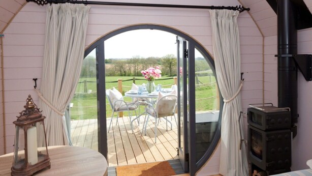 A cozy room with a large arched window, a wooden deck, a table with chairs, and a fireplace. - Wonderful  villa for 4 guests with hot tub, terrace and pets allowed (Banbury)