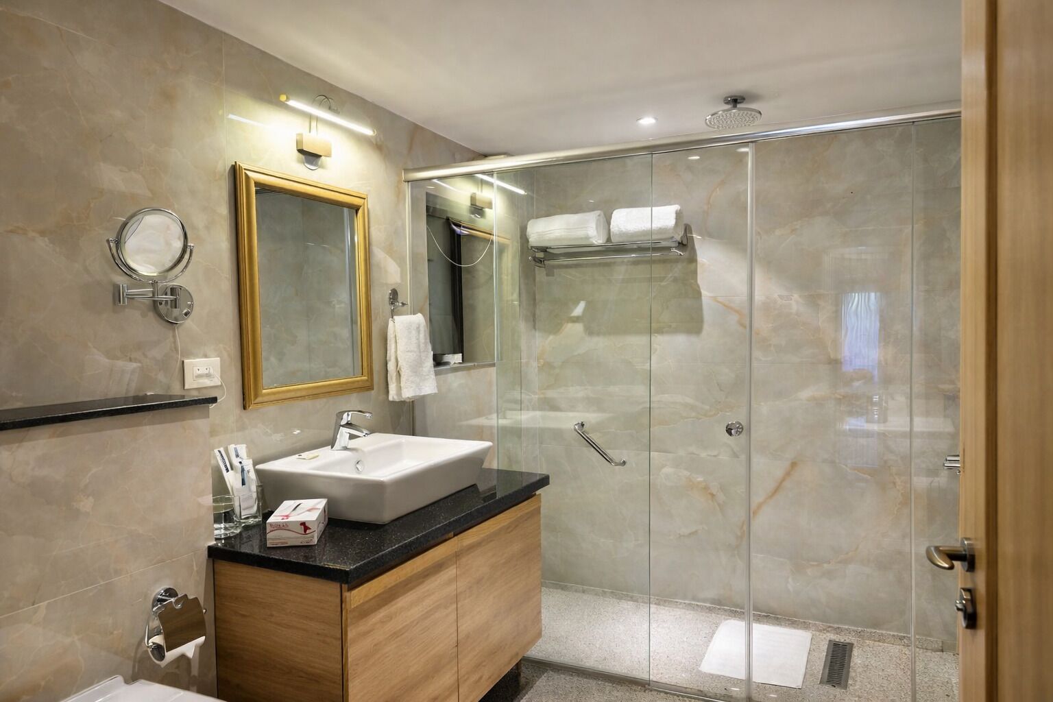 A modern bathroom with a glass-enclosed shower, a large mirror, and a vanity with a sink and towel rack.