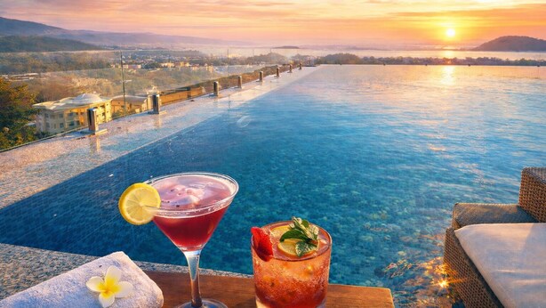 Une vue sur la piscine au coucher du soleil, deux boissons et une serviette.