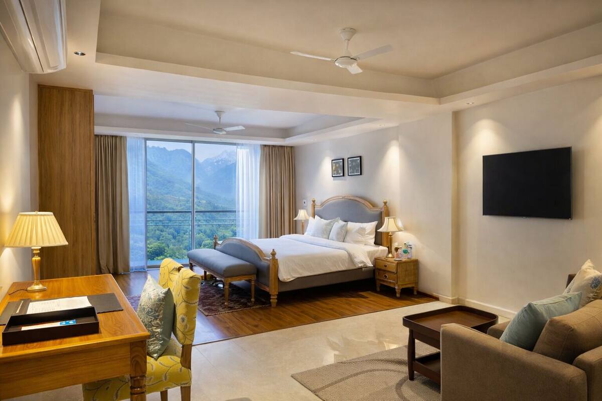 A hotel room with a bed, a desk, a chair, a TV, and a view of the outdoors.