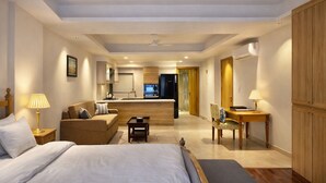 Une chambre d’hôtel avec un lit, un canapé, un bureau et, au fond, une petite cuisine.