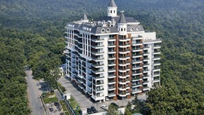 Un hôtel à plusieurs étages, doté d’une tour centrale, entouré d’une végétation luxuriante et de montagnes.
