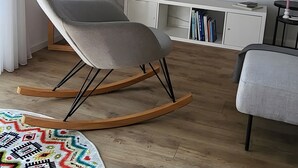 Un salon moderne avec un fauteuil à bascule gris, un téléviseur à écran plat, un meuble blanc et une plante en pot.