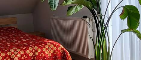 A room with a bed, a radiator, a potted plant, and a window with curtains.