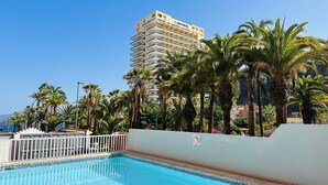 A hotel pool area with a clear blue pool, surrounded by palm trees and a high-rise building in the background. - Pink Alta Apartment With Pool (Puerto de la Cruz)