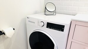 A front-loading LG washing machine with a control panel, a toilet paper holder, and a pink cabinet. - Pink Alta Apartment With Pool (Puerto de la Cruz)