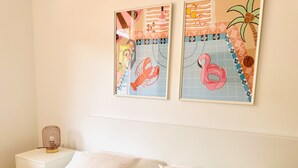 A bedroom with a bed, two pillows, a nightstand, and two wall-mounted artworks depicting a lobster and a flamingo. - Pink Alta Apartment With Pool (Puerto de la Cruz)