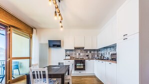 A modern kitchen with white cabinets, a wooden dining table, and chairs. - Beautiful apartment for 4 guests with A/C, TV and patio (Torri Del Benaco)