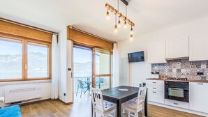 A modern kitchen with white cabinets, a black countertop, and a tiled backsplash. There is a dining area with a table and chairs, and a balcony with a view of the mountains. - Beautiful apartment for 4 guests with A/C, TV and patio (Torri Del Benaco)