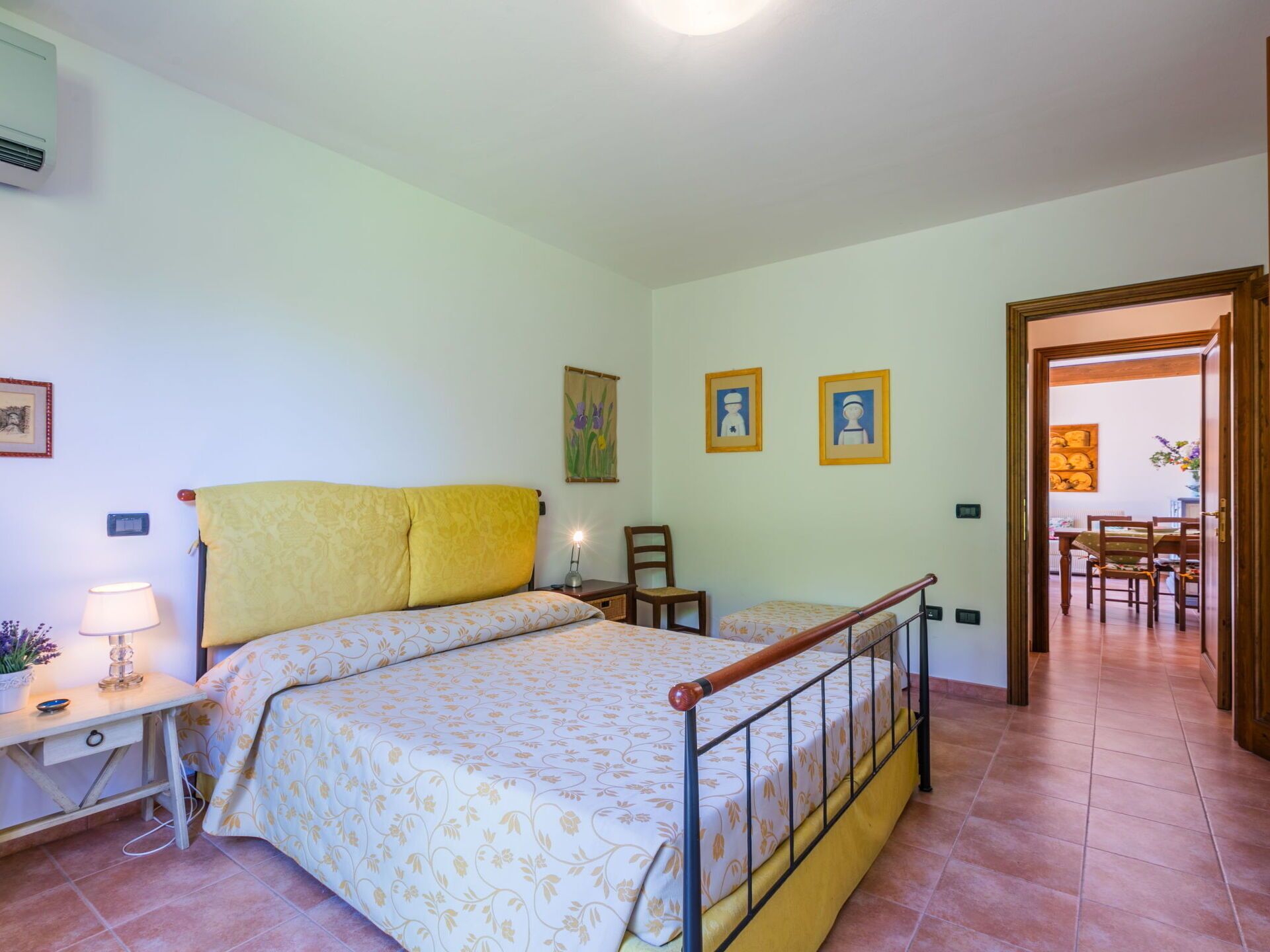 A bedroom with a bed, bedside table, lamp, and a door leading to a dining area.