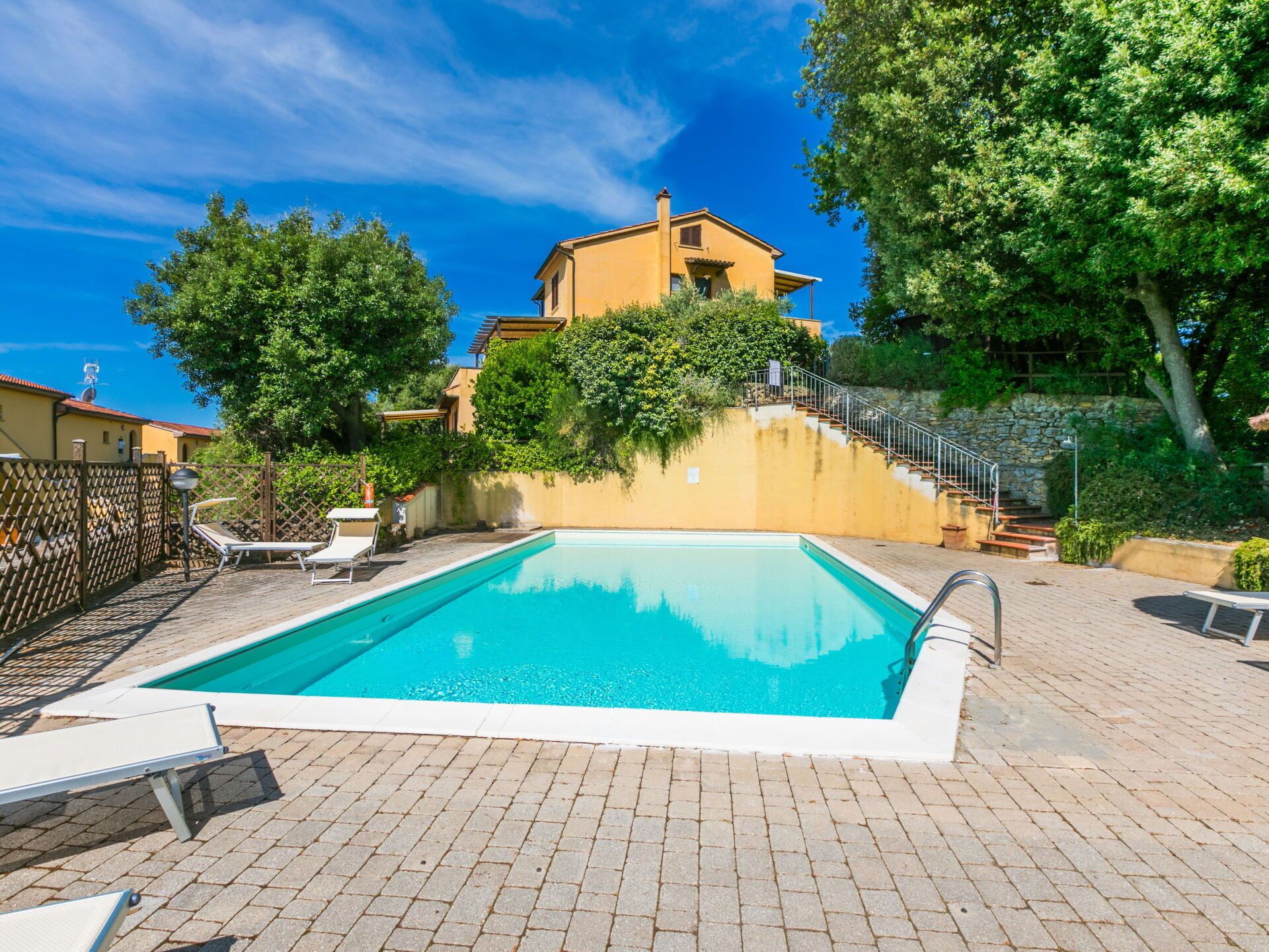 Une piscine avec des chaises longues, un escalier en pierre et un bâtiment à la façade jaune.