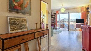 Ein Wohnzimmer mit einem Holztisch, einem Bücherregal, einem Gemälde und Blick ins Freie durch eine Glastür.