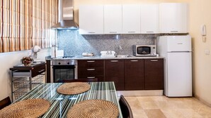 A modern kitchen with dark wooden cabinets, a white refrigerator, a microwave, and a stove. There is a dining table with striped placemats and a basket of oranges. - Céntrico Apartamento en Santa Cruz (Santa Cruz de Tenerife)