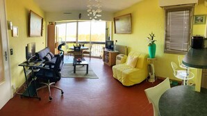 A living room with a sofa, a TV, and a dining area with chairs and a table. - Large, comfortable T2 apartment (Mauguio)