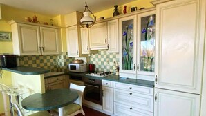 A kitchen with white cabinets, a microwave, a stove, and a dining area with a table and chairs. - Large, comfortable T2 apartment (Mauguio)