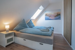 A bedroom with a loft bed, a skylight, a nightstand, and a painting on the wall.