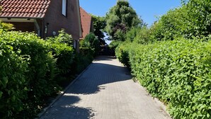 A paved pathway flanked by greenery and a building with a red-tiled roof.