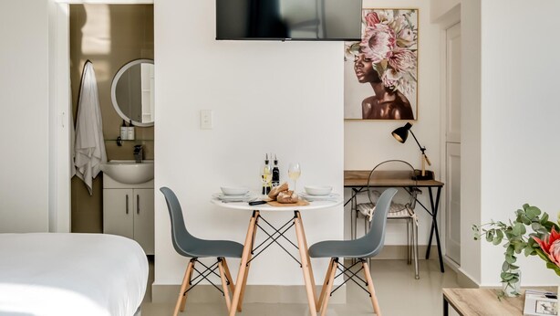 Une chambre d’hôtel moderne comprenant un lit, une table à manger avec des chaises, un téléviseur fixé au mur, un miroir et un tableau.