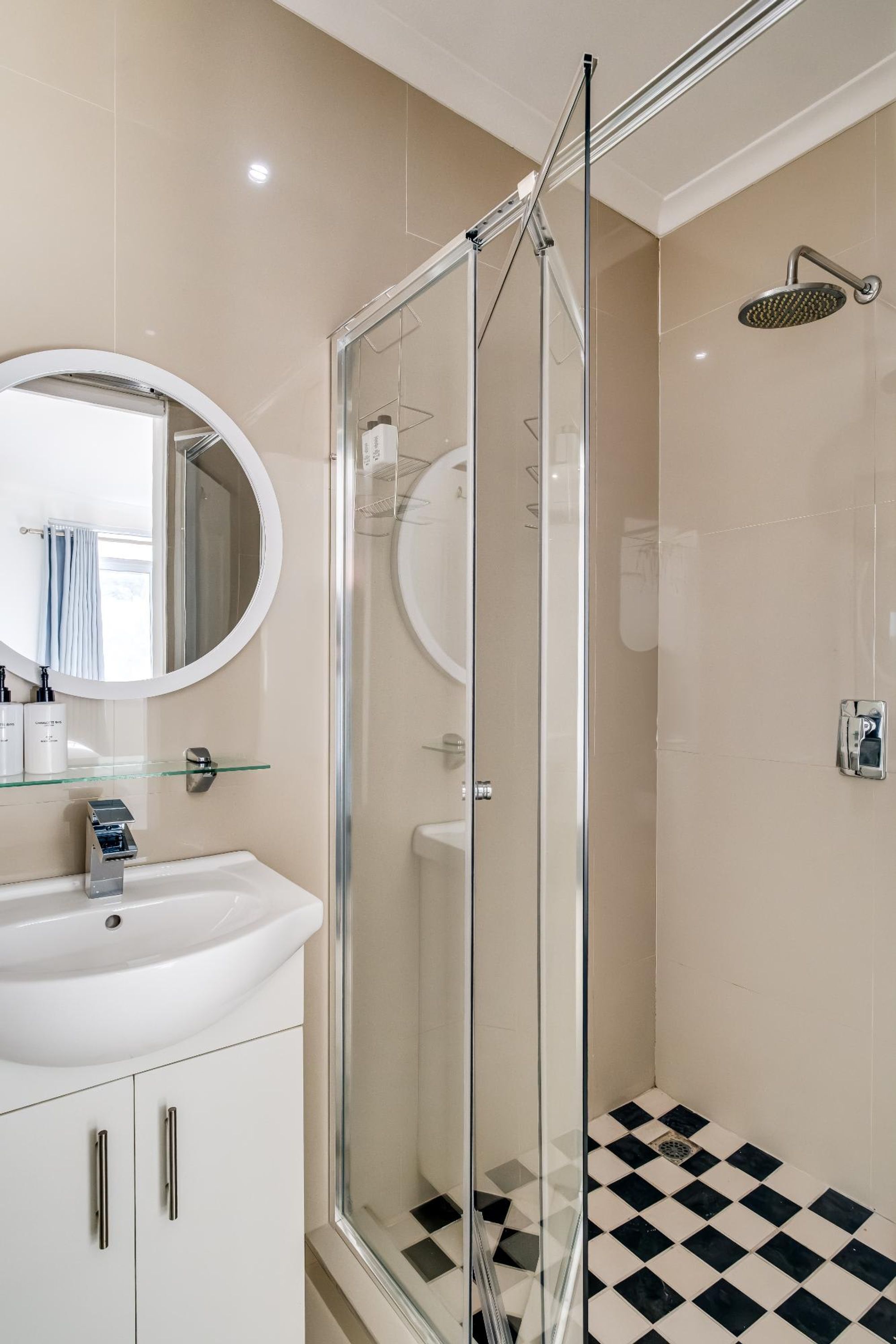 A modern bathroom with a glass-enclosed shower, a round mirror, and a white sink.