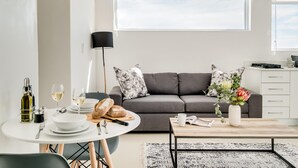 Un salon moderne avec un canapé gris, une table à manger avec des assiettes et des verres, une table basse ornée d’un vase de fleurs et un lampadaire.