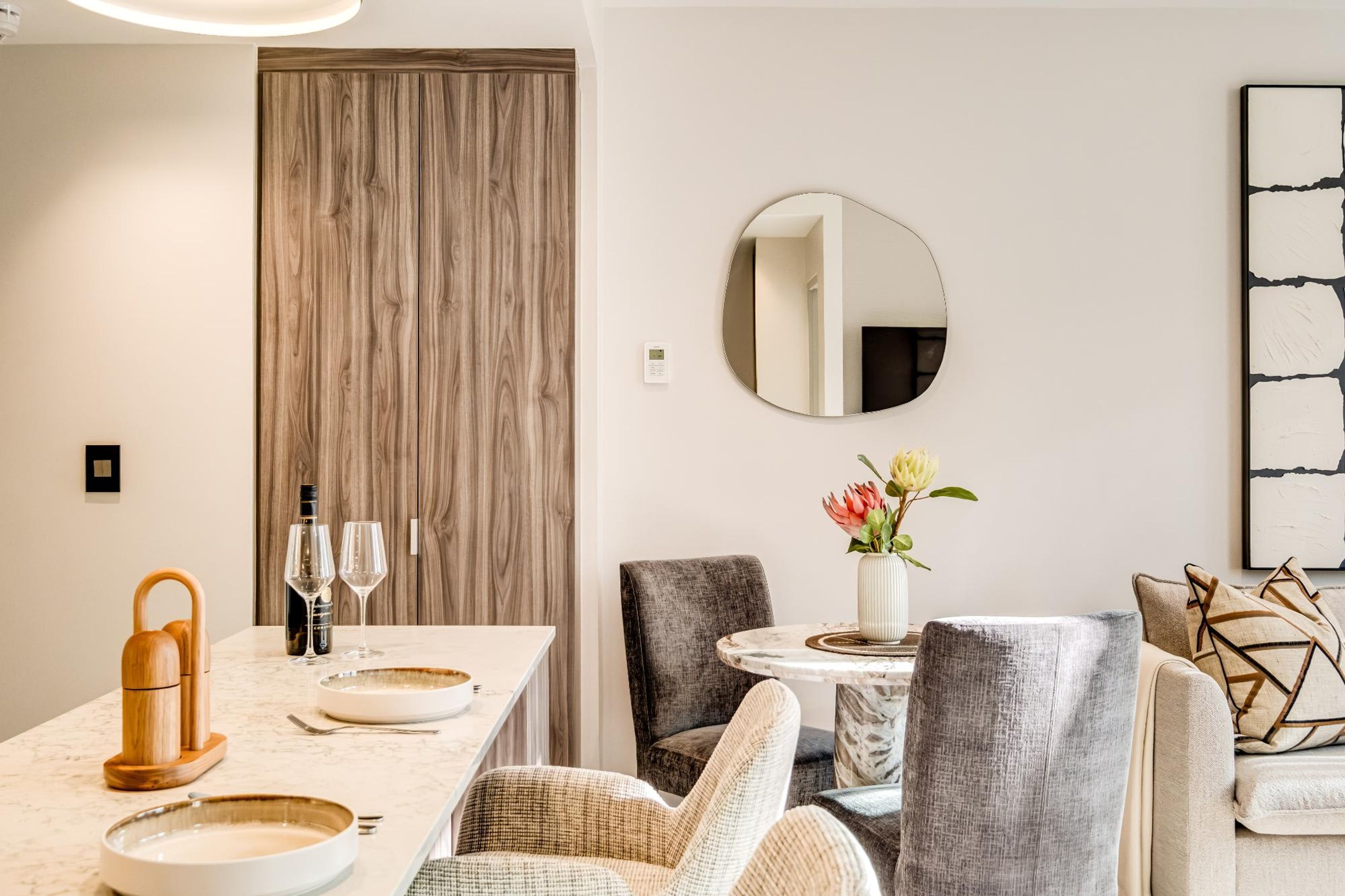 A dining area with a wooden door, a round mirror, and a table set with plates and glasses.