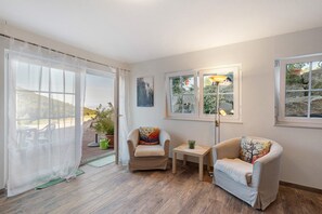 Una habitación con un ventanal grande, una silla, una mesita y una lámpara.
