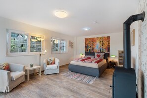 Un dormitorio moderno con cama, dos sillones, una mesita, chimenea y ventanas amplias.