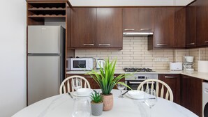 A modern kitchen with wooden cabinets, a built-in microwave, and a dining table set for two. - Apollo 2-Bedroom Apartment in Larnaca (Larnaca)