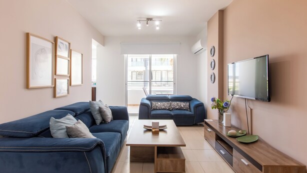 A modern living room with a sofa, a coffee table, a TV, and framed artwork on the wall. - Apollo 2-Bedroom Apartment in Larnaca (Larnaca)