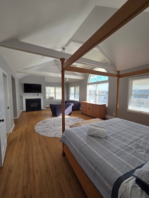 A bedroom with a four-poster bed, a fireplace, a television, and a view of the city.